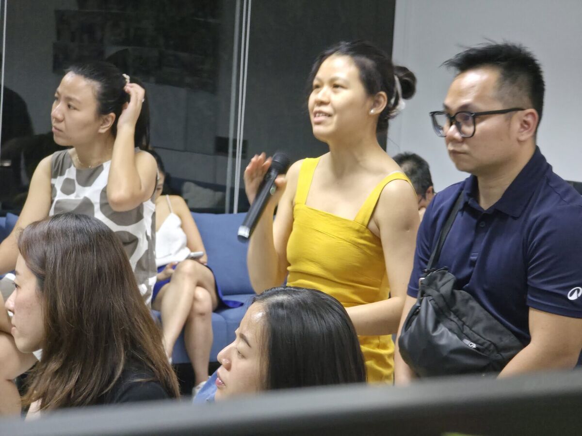 An attendee standing with a microphone to ask a question at an AI Power Users meetup in Singapore, with the seated audience around her